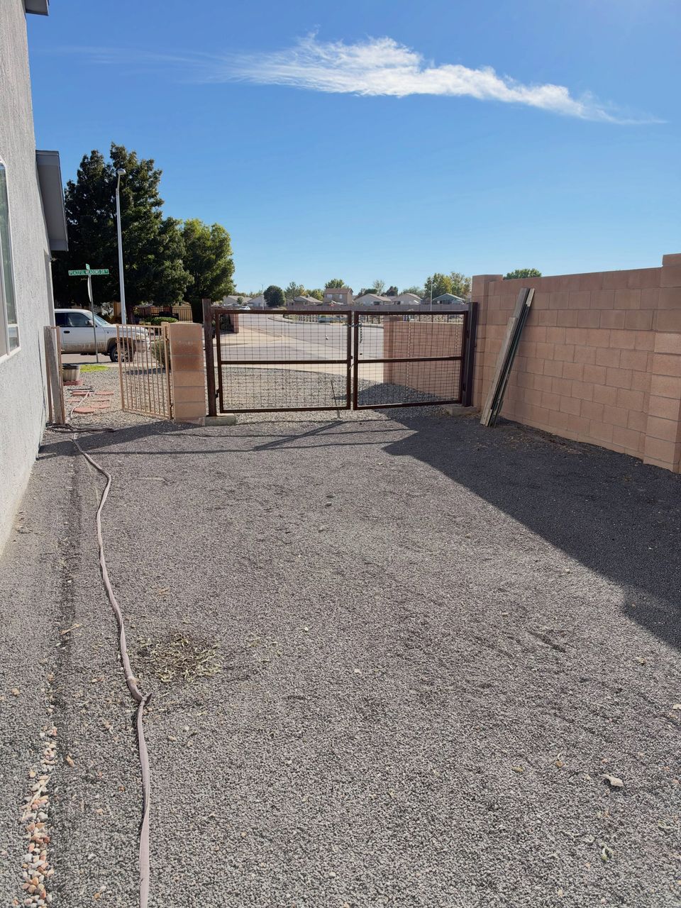 A long gravel driveway along a block wall, swept clear up to the iron gate.