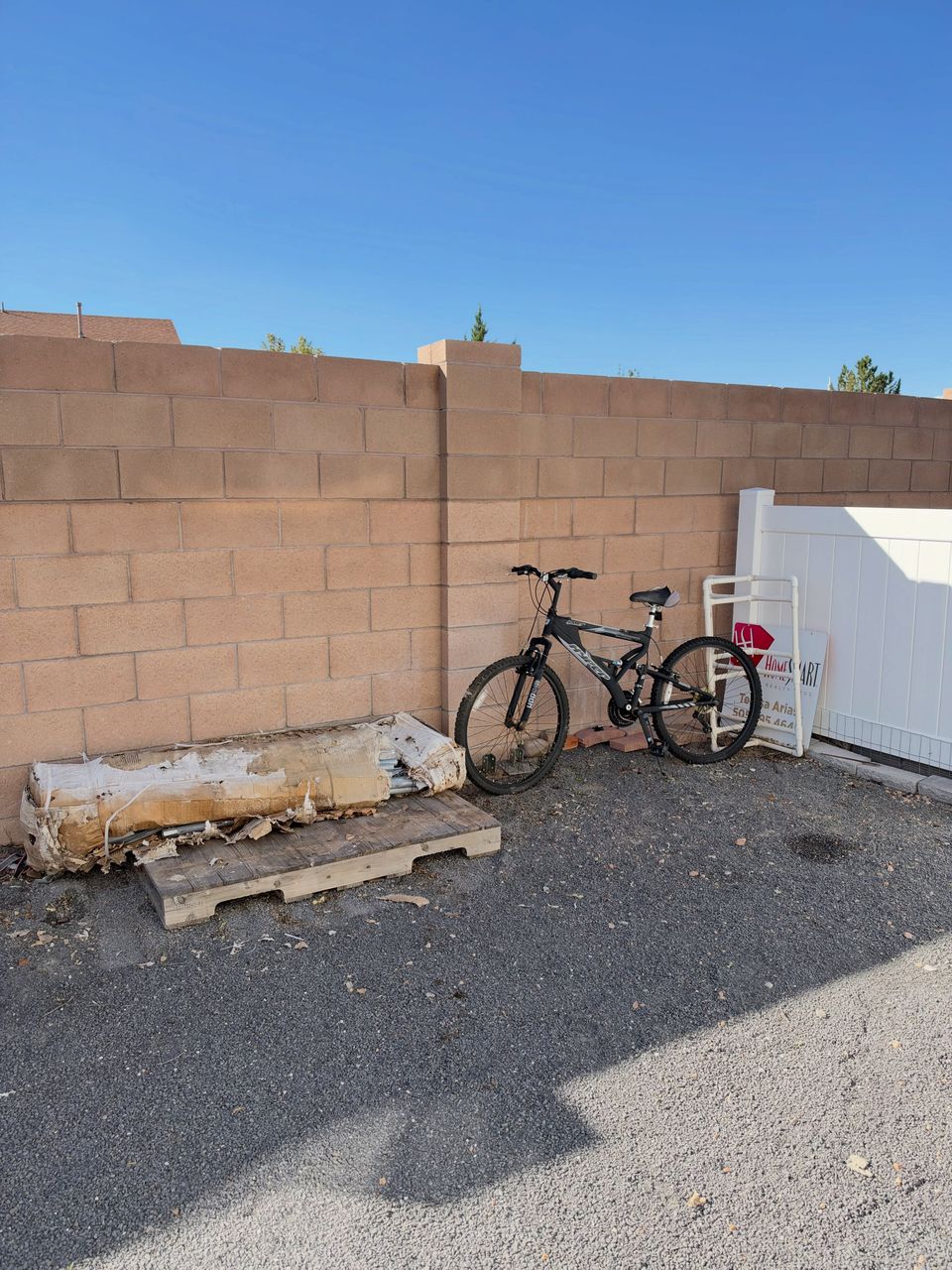The same corner after the haul: brush, chair and debris gone, just a bike against the block wall.
