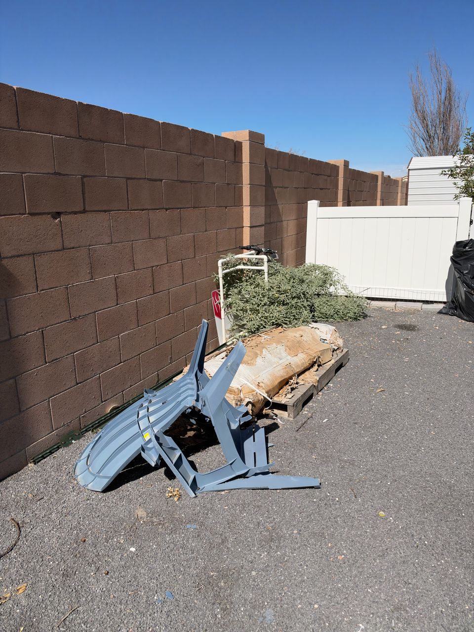 A pile of brush, a broken plastic chair and debris against a block wall at the end of a driveway, before the haul.