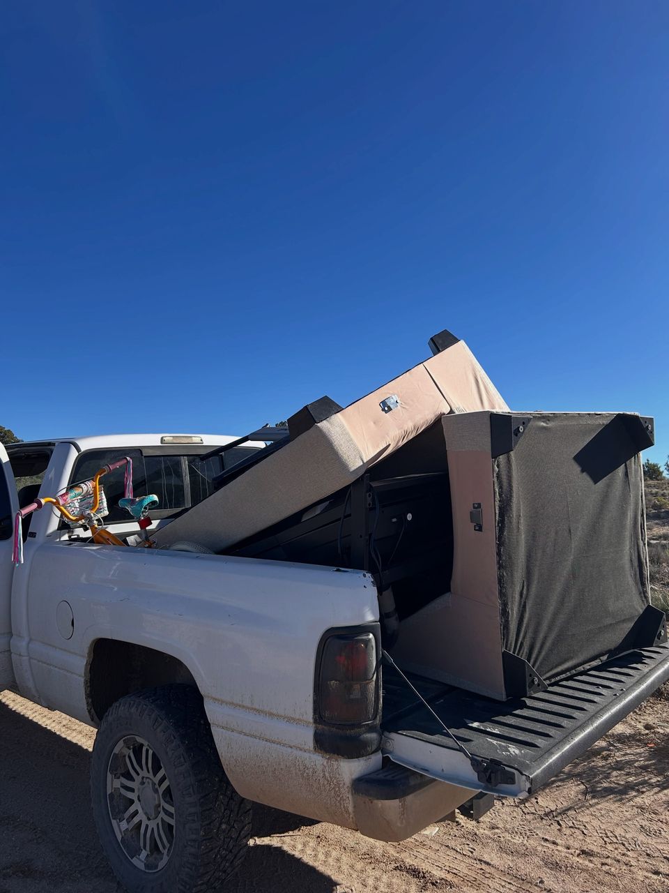 A white pickup loaded high with an old couch, a mattress and furniture, tailgate down, under a deep blue sky.